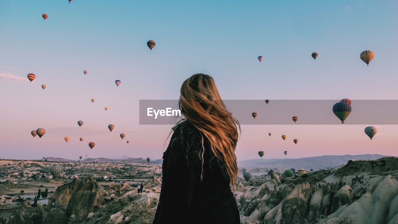 REAR VIEW OF WOMAN IN HOT AIR BALLOON AGAINST SKY