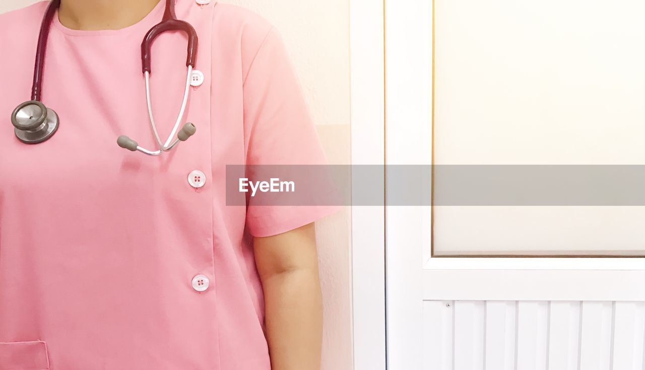 Midsection of female doctor with stethoscope standing by doorway