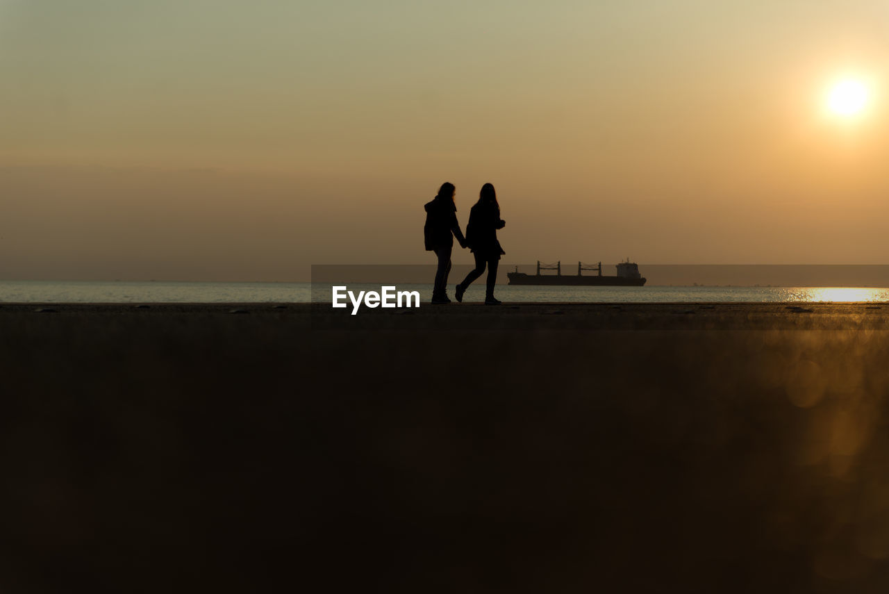 Silhouette couple standing on beach against sky during sunset