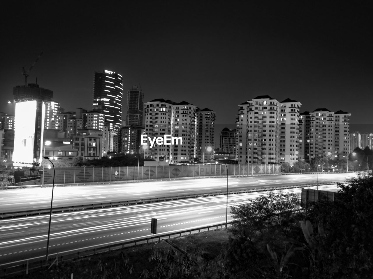 Light trails over road against illuminated buildings at night