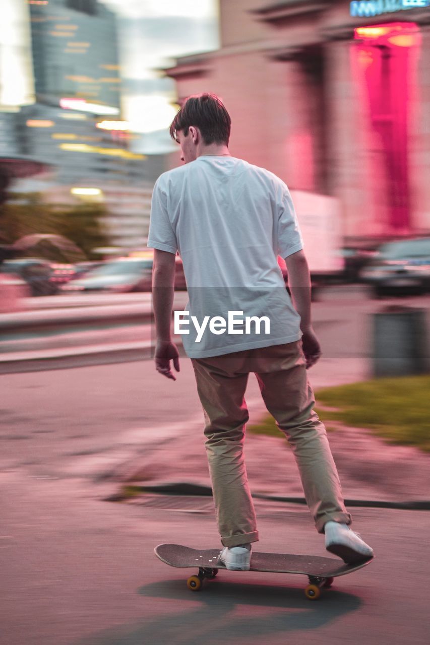 Rear view of man skateboarding on road in city