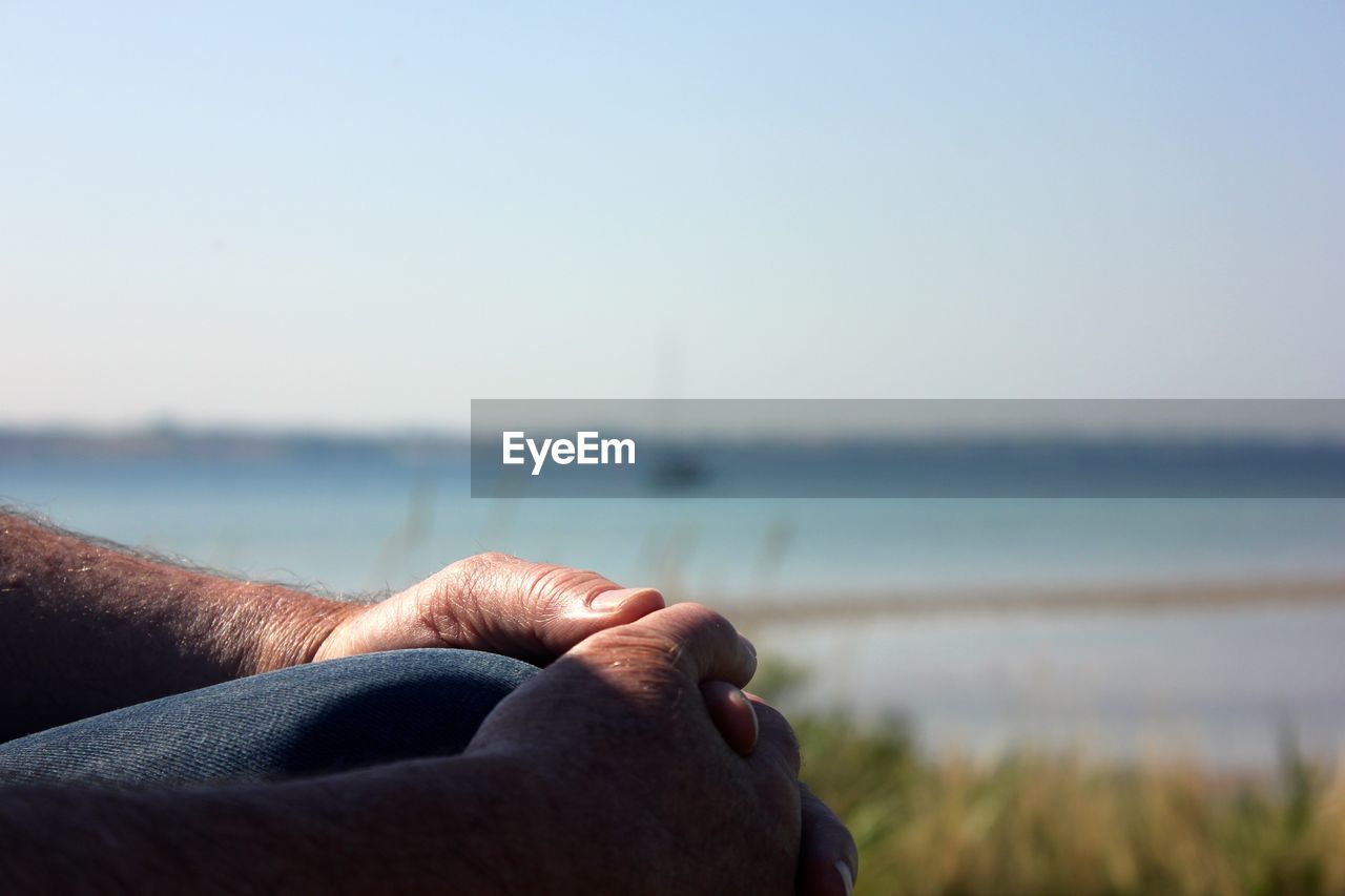 Close-up of person sitting outdoors against sky