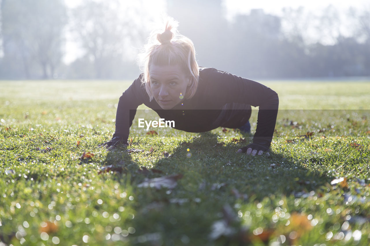 Confident woman doing push-ups on grassy field at park during sunny day