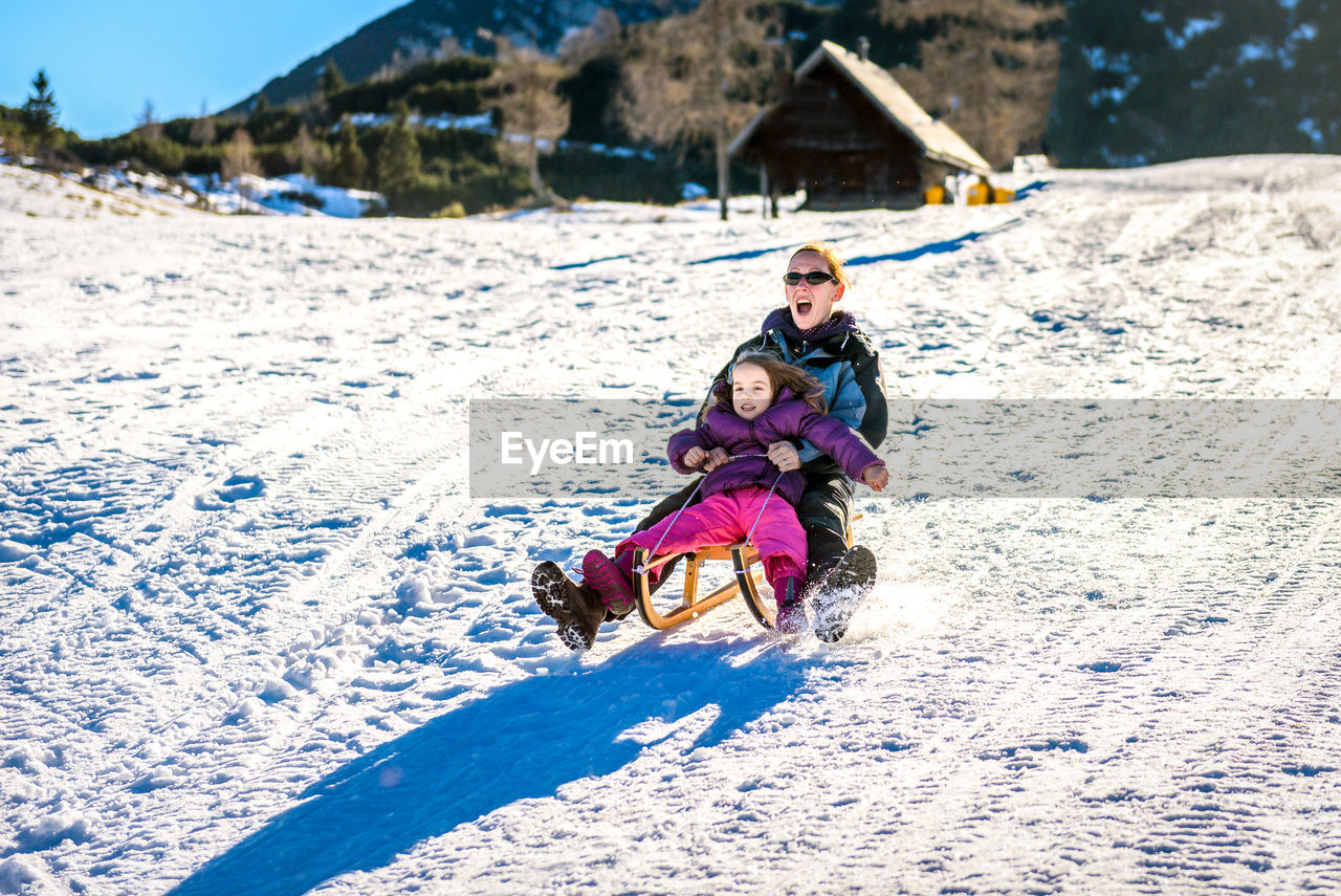 Portrait of mother and daughter sliding on snow