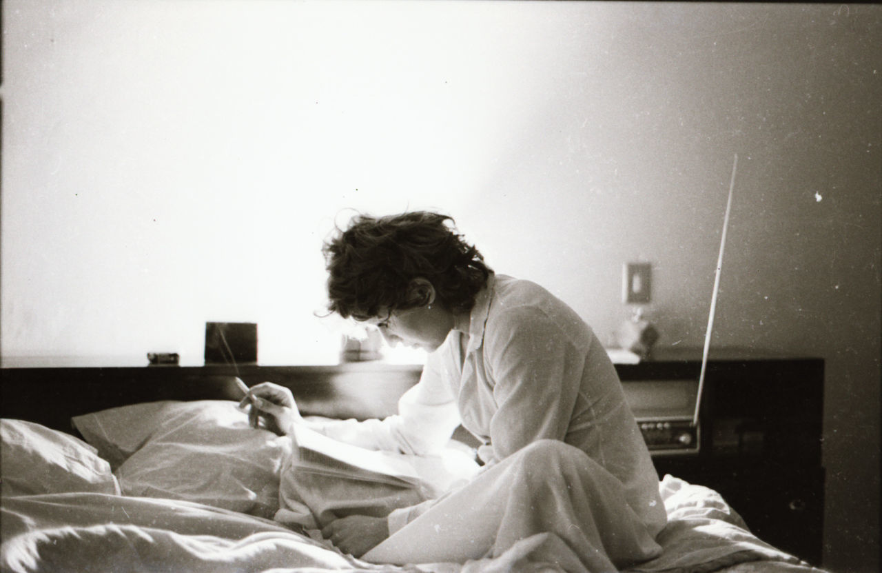 YOUNG WOMAN SITTING ON BED IN BEDROOM