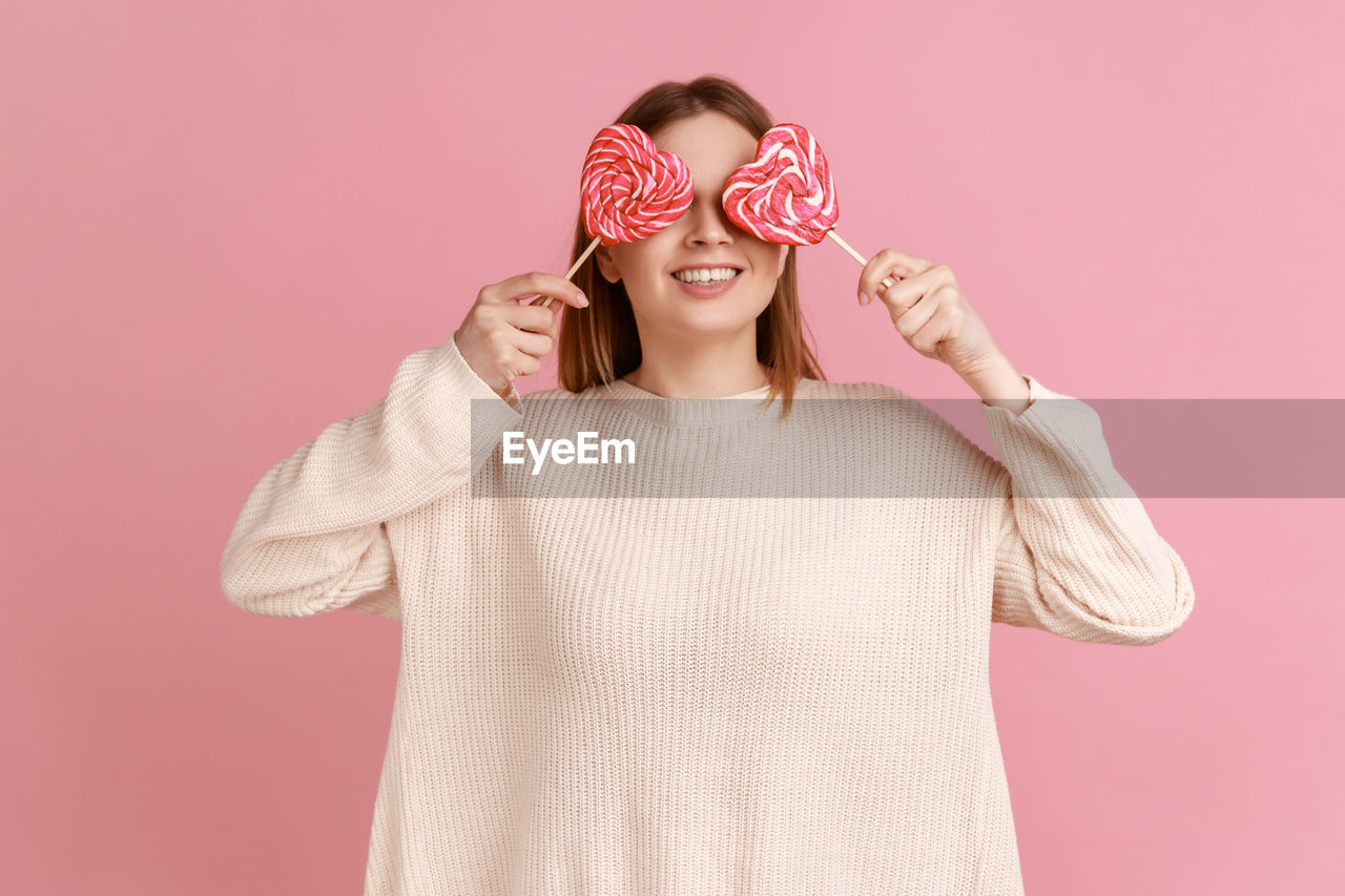 Woman holding lollipop against pink background