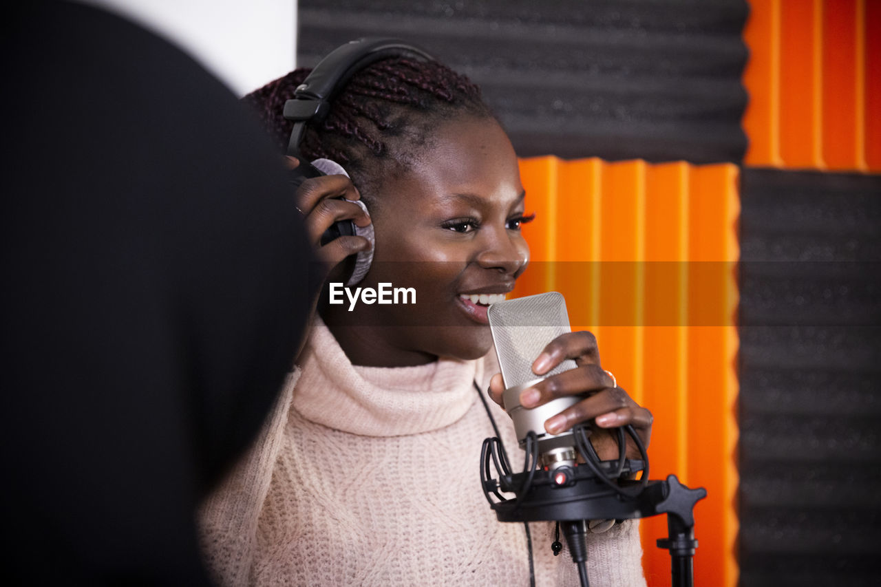 Smiling singer adjusting headphones while recording song in studio