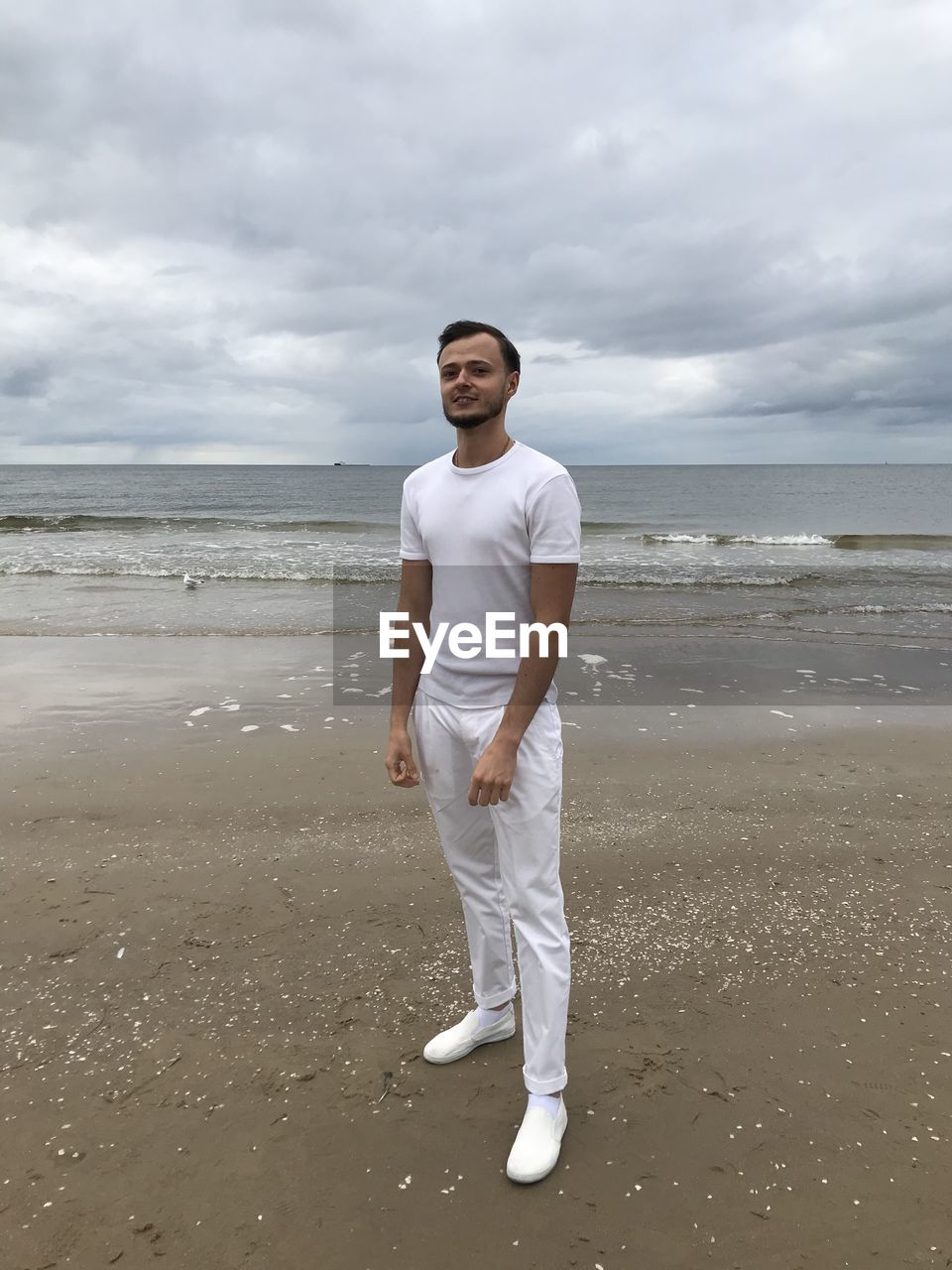 FULL LENGTH OF YOUNG MAN STANDING AT BEACH