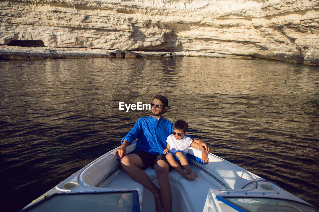 Father and son swim on the bow of a high-speed motor boat in the summer near  rocky coast in crimea