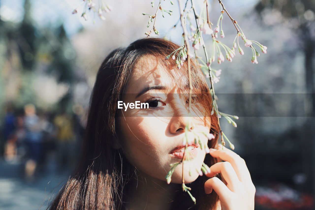 Close-up portrait of young woman with flower buds at park