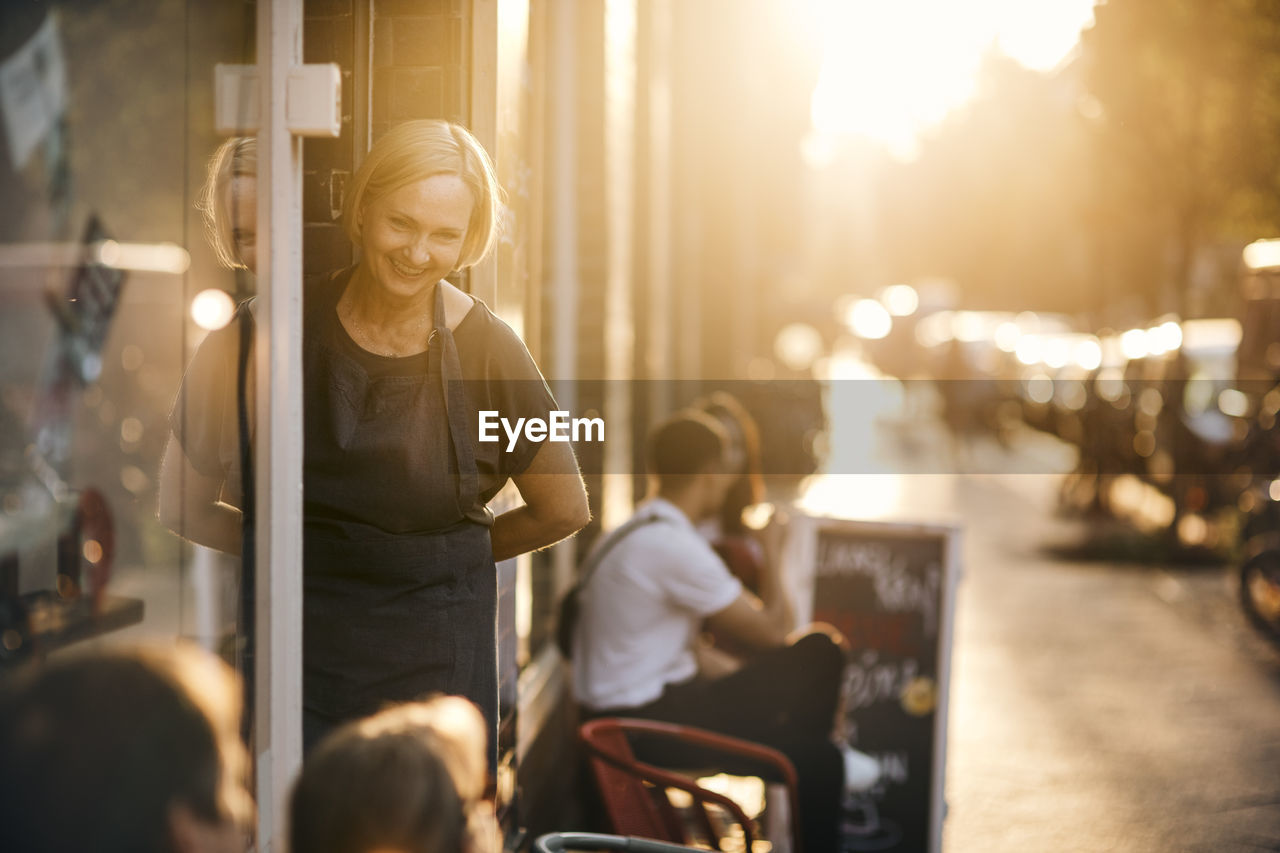 Portrait of smiling female employee standing at entrance of deli