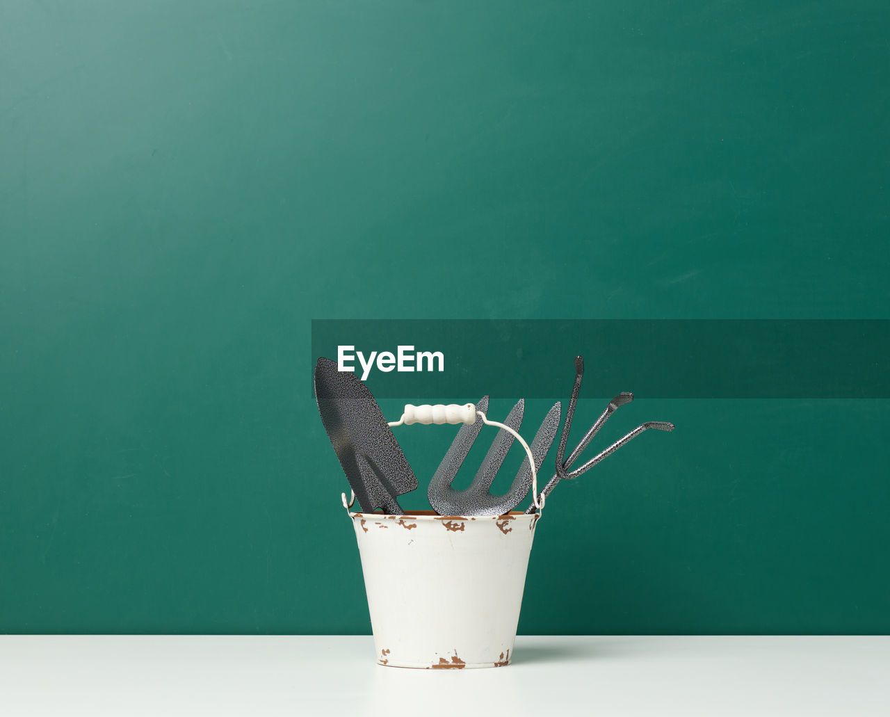 Miniature garden tools in a metal bucket on a green background, copy space