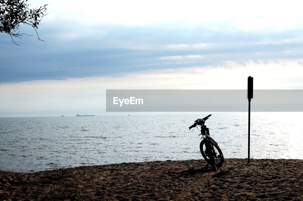 PERSON RIDING BICYCLE ON BEACH AGAINST SKY