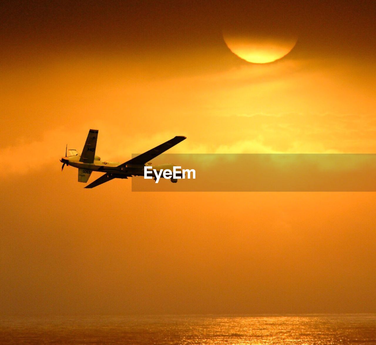 AIRPLANE FLYING OVER SEA DURING SUNSET