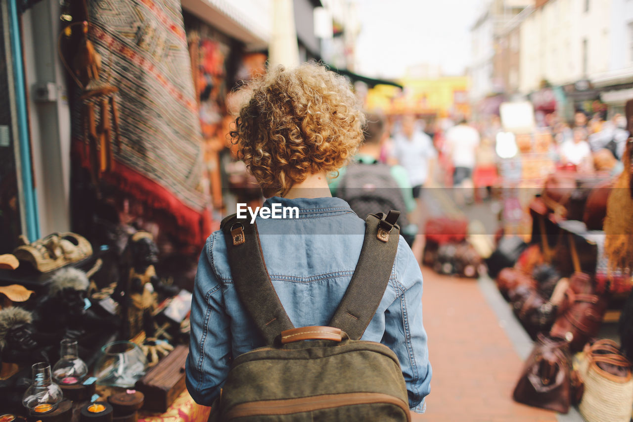 Rear view of woman walking through street market stalls in city