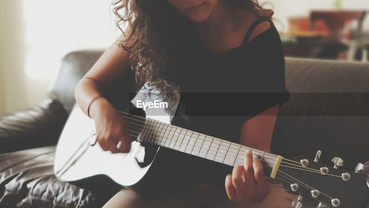 Midsection of woman playing guitar on sofa at home