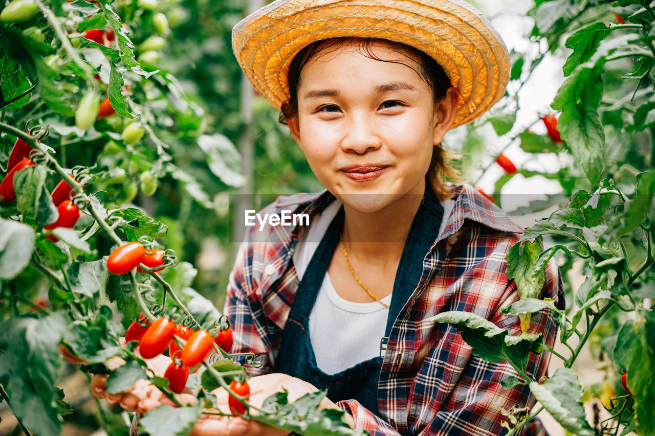 portrait of smiling young woman wearing hat standing by plants