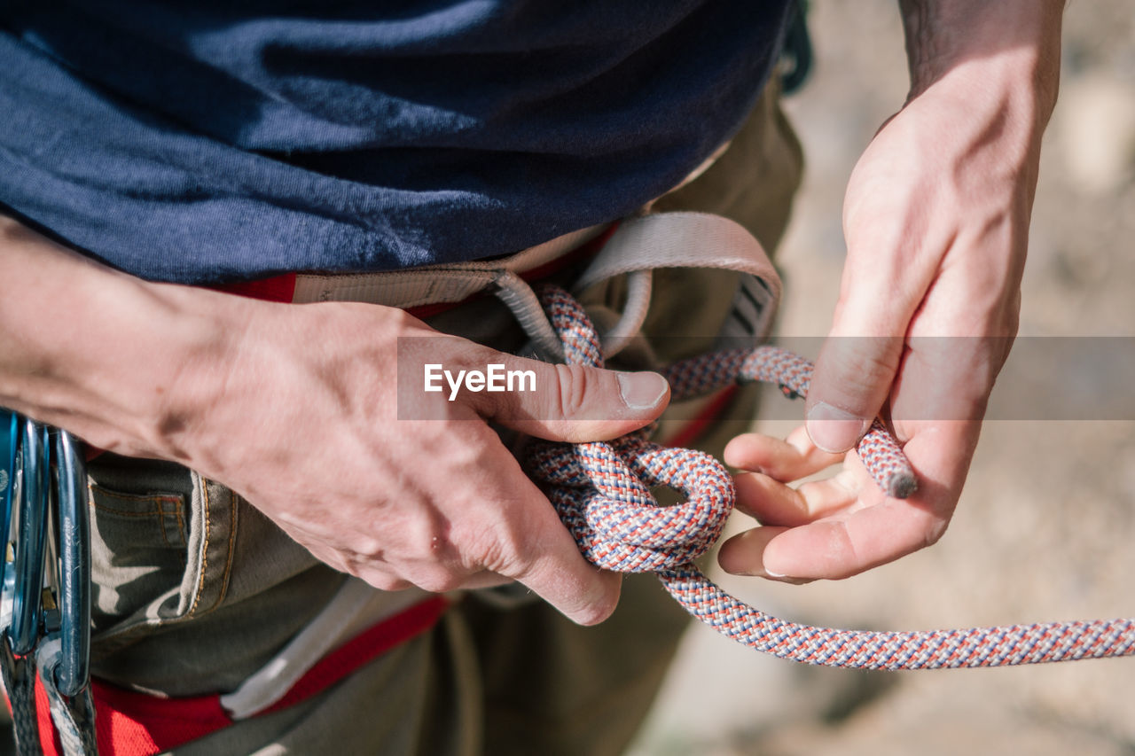 Midsection of male climber tying rope