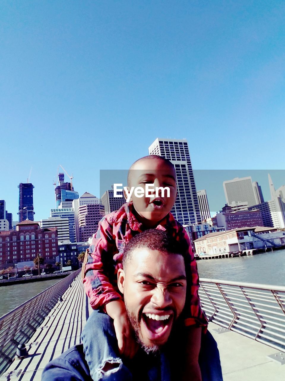 Portrait of father carrying son in city against clear sky