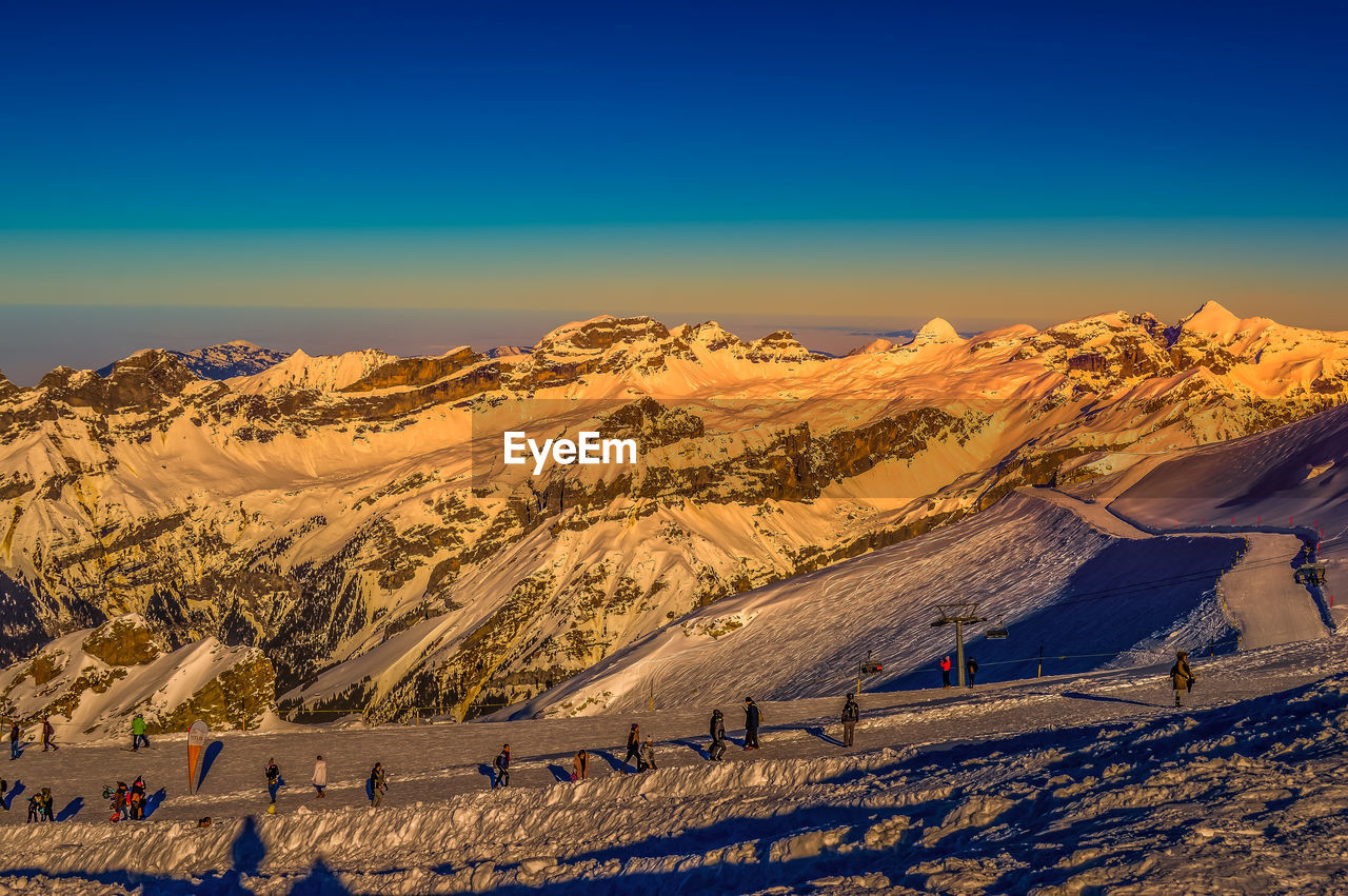 PEOPLE ON SNOWCAPPED MOUNTAIN AGAINST BLUE SKY