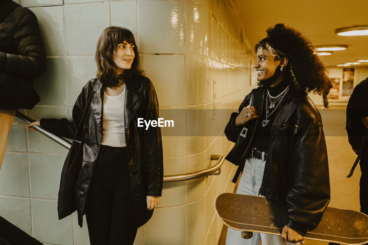 Smiling female friends looking at each other in illuminated subway