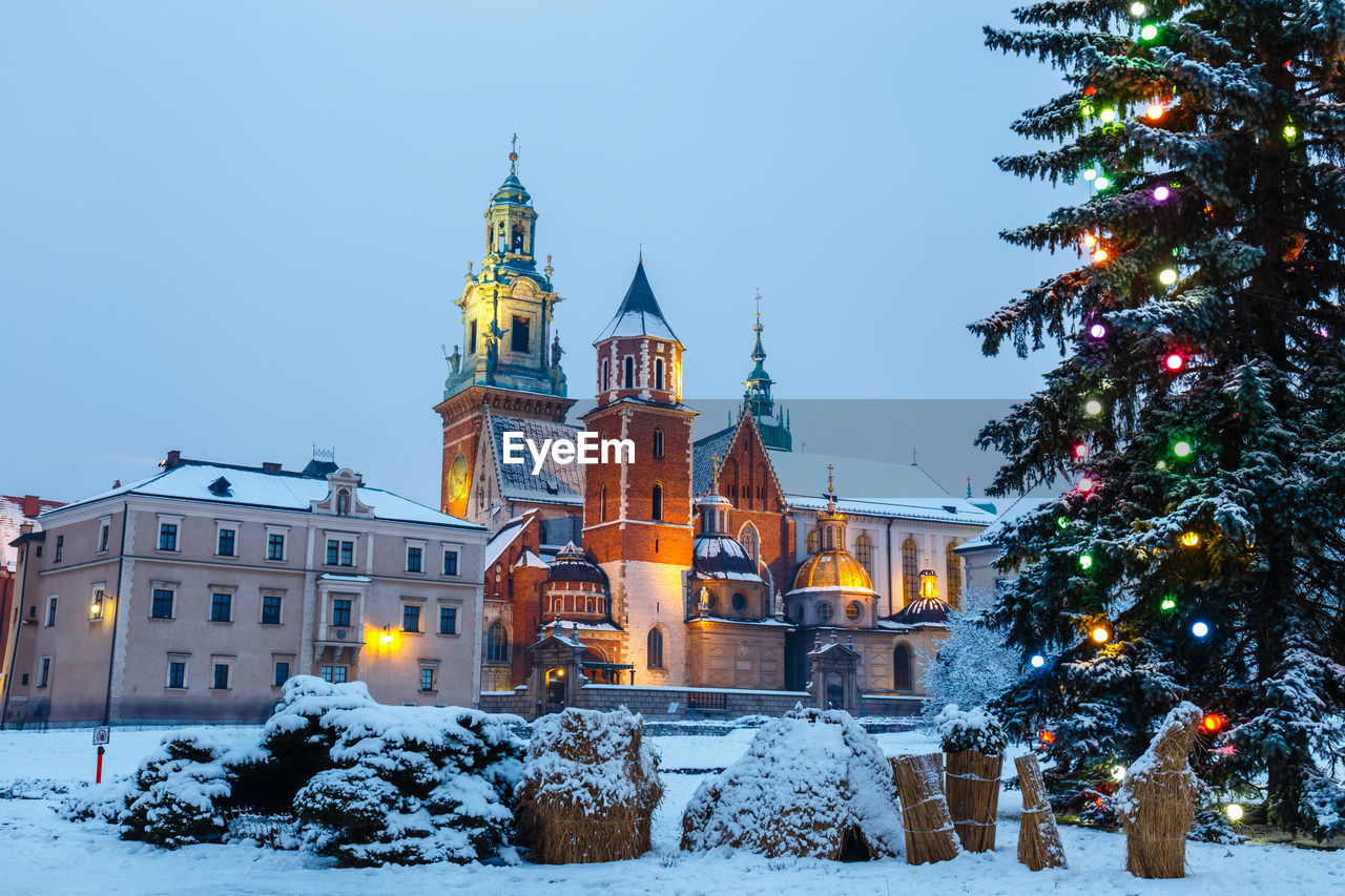 ILLUMINATED CHRISTMAS TREE AGAINST BUILDING IN WINTER