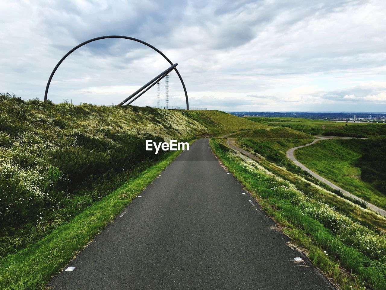 Horizon observatory on field by road against cloudy sky