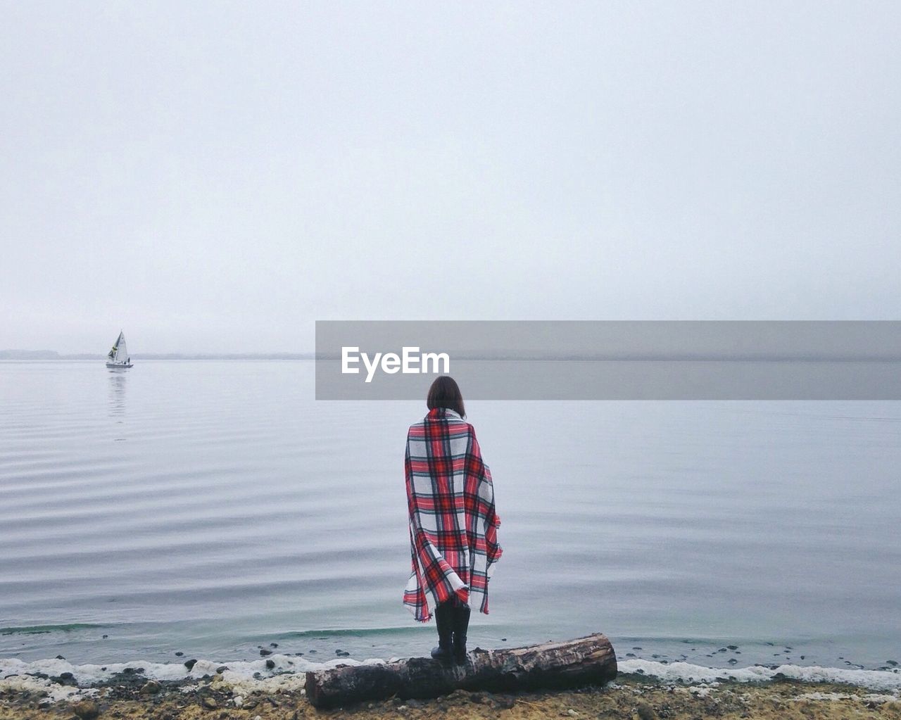 Rear view of woman standing at sea shore during foggy weather