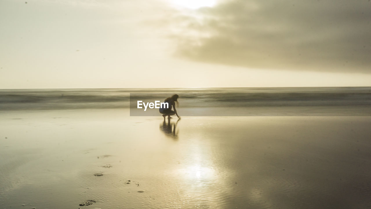 Side view of woman crouching at beach