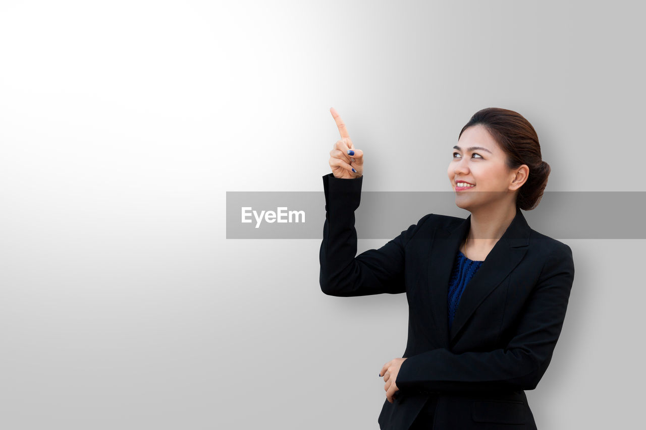 Businesswoman smiling while pointing against gray background