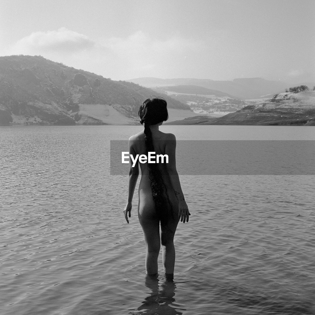 Rear view of naked woman standing in lake