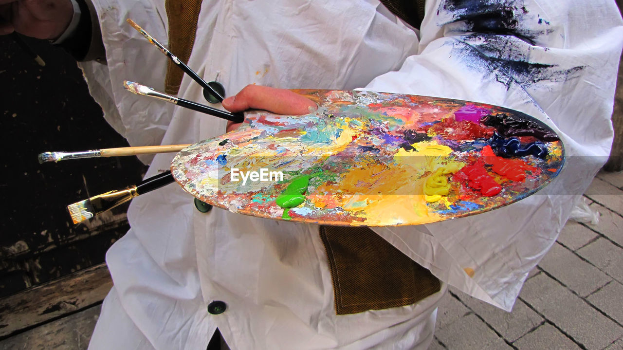 Close-up of hand holding painting brushes and messy palette