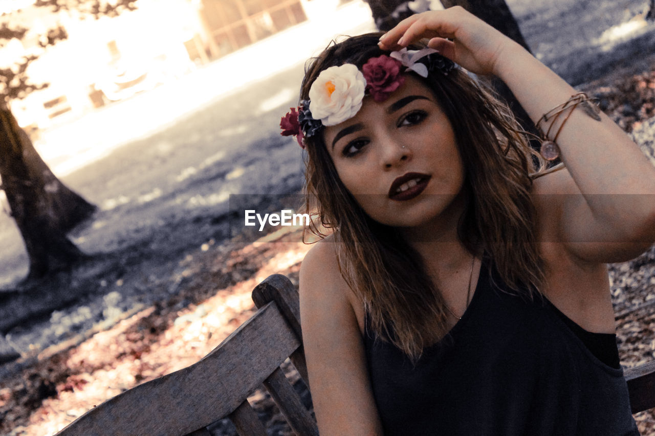 Portrait of young woman wearing flowers while sitting on bench at park