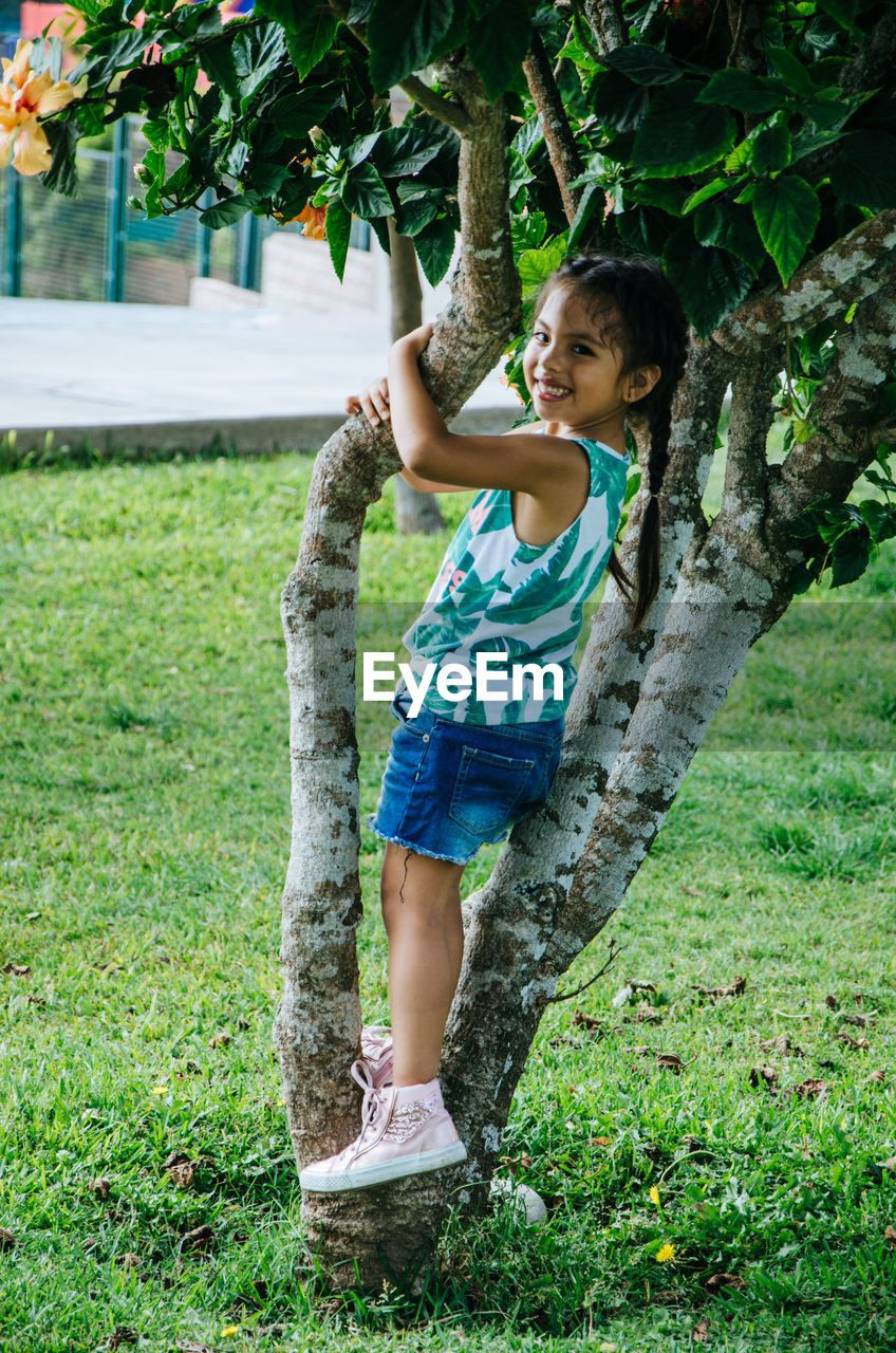 Side view portrait of girl smiling while standing on tree at park