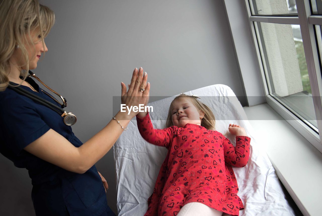 Pediatrician high-fiving with cute girl in medical clinic