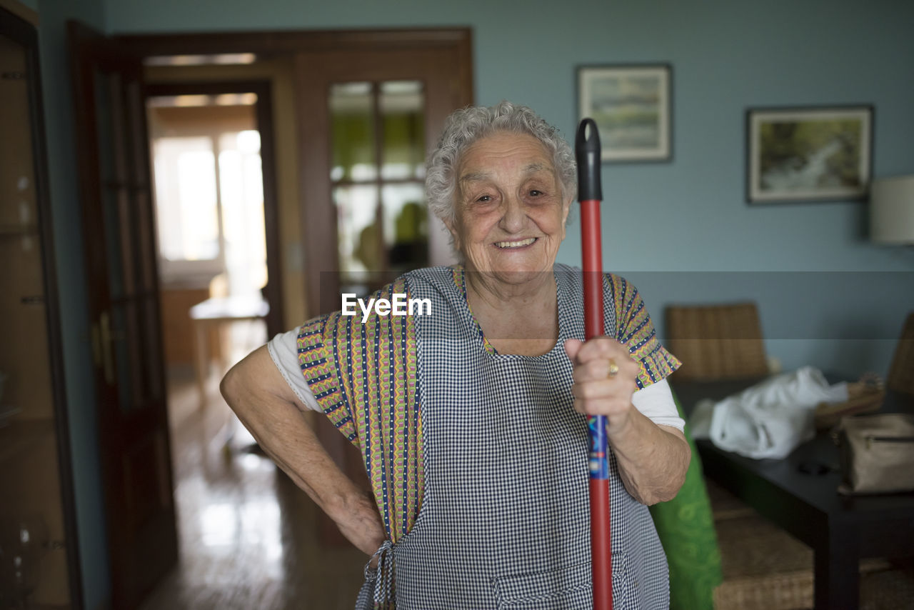 Portrait of smiling senior woman holding stick of cleaning mop