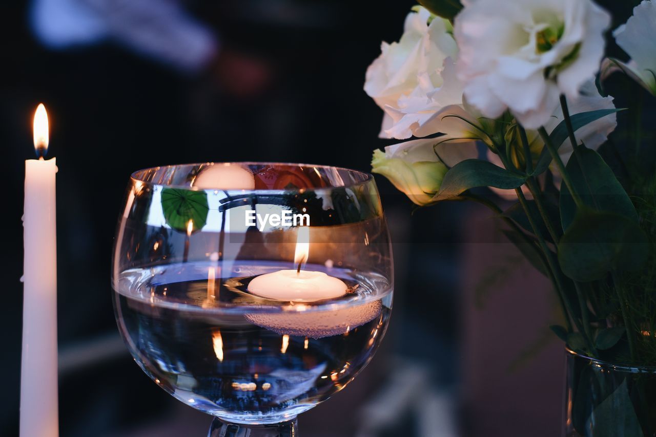 CLOSE-UP OF LIT CANDLES ON GLASS