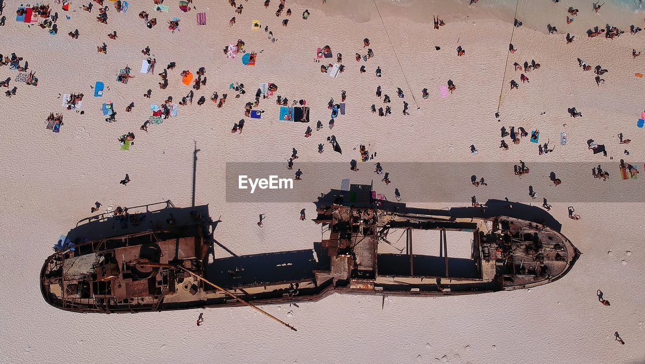 Drone view of people by abandoned ship at beach
