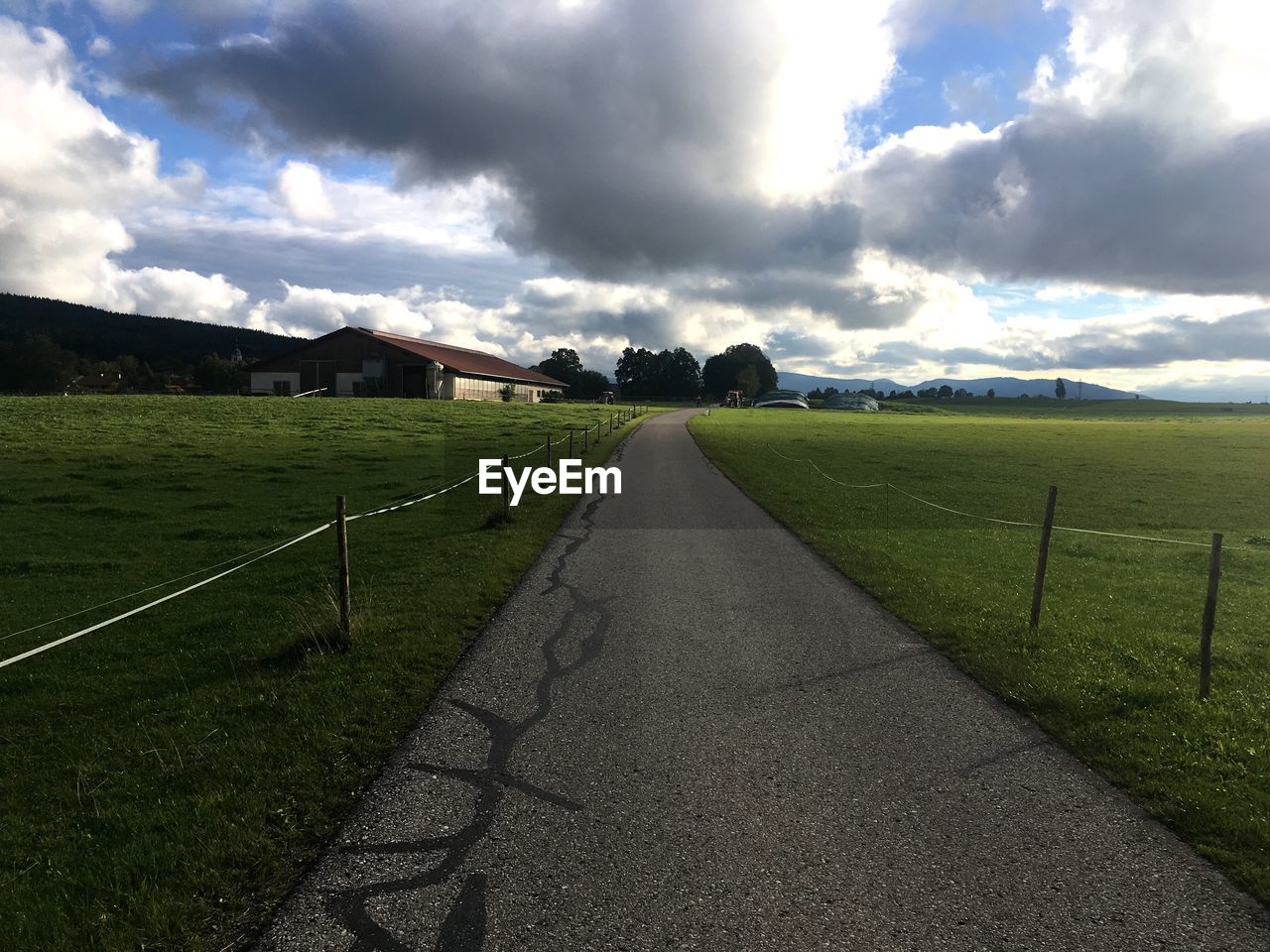 EMPTY COUNTRY ROAD ALONG LANDSCAPE AND AGAINST CLOUDY SKY