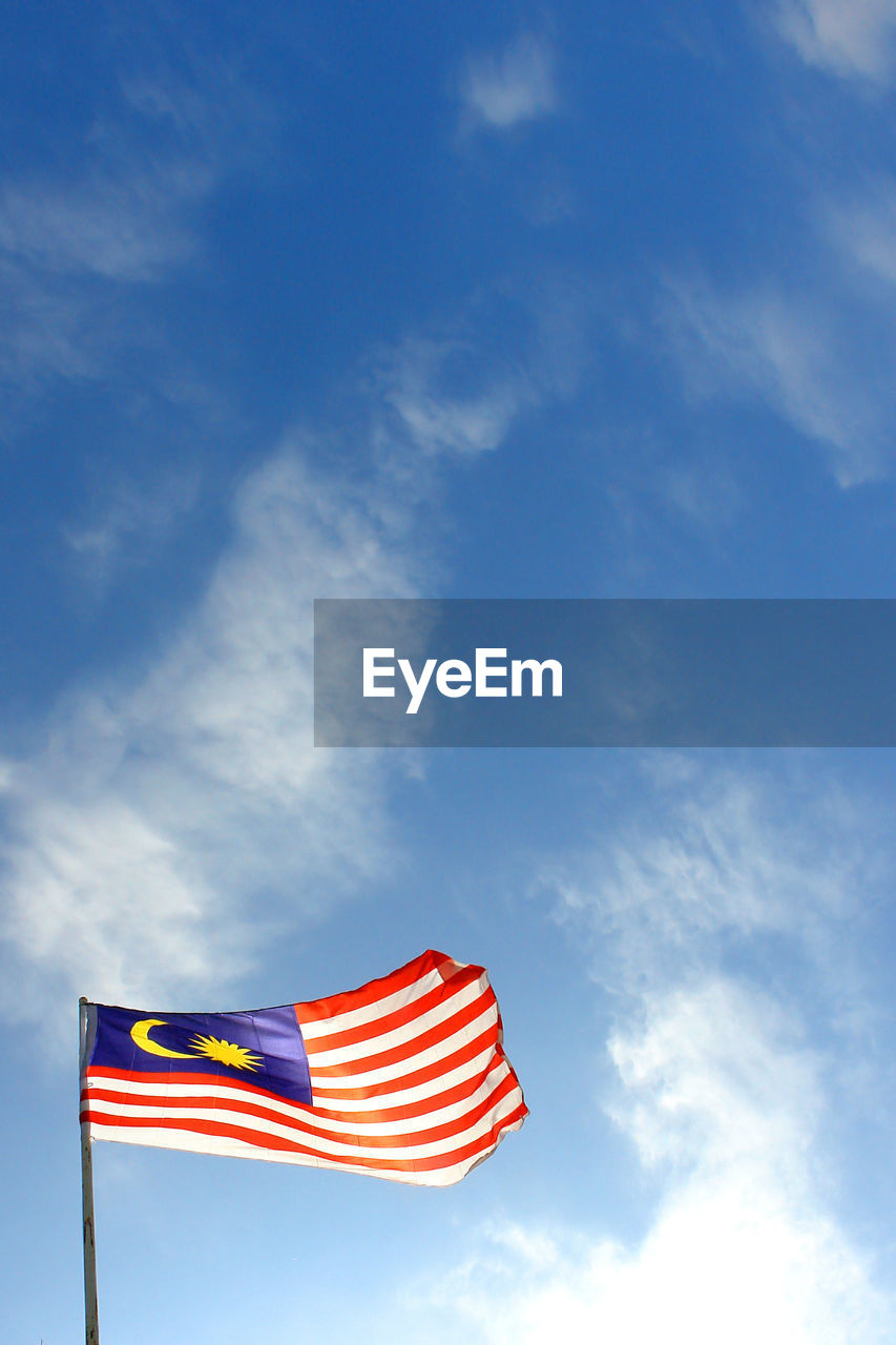Low angle view of malaysian flag waving against blue sky
