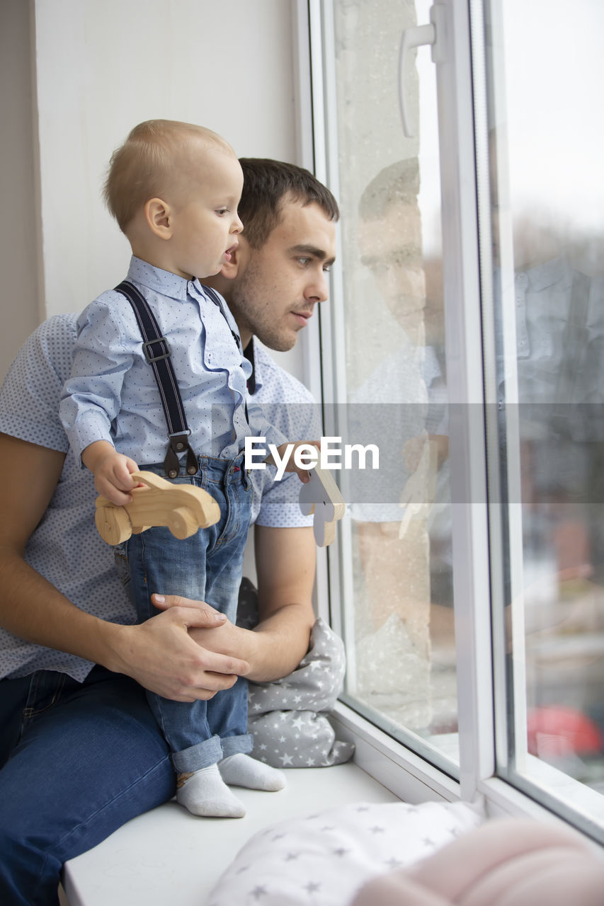 Father and son looking through window at home