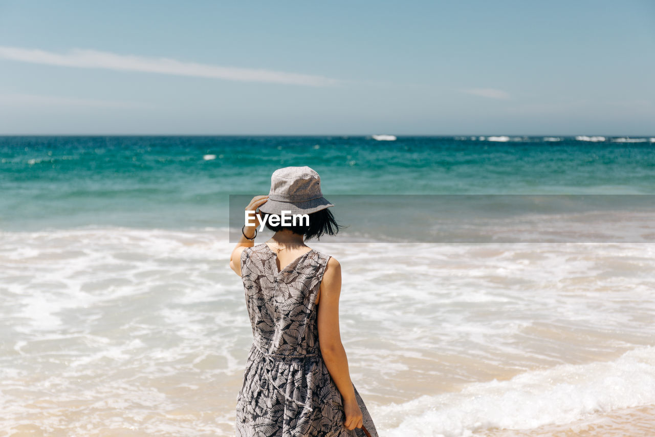 REAR VIEW OF WOMAN STANDING ON BEACH