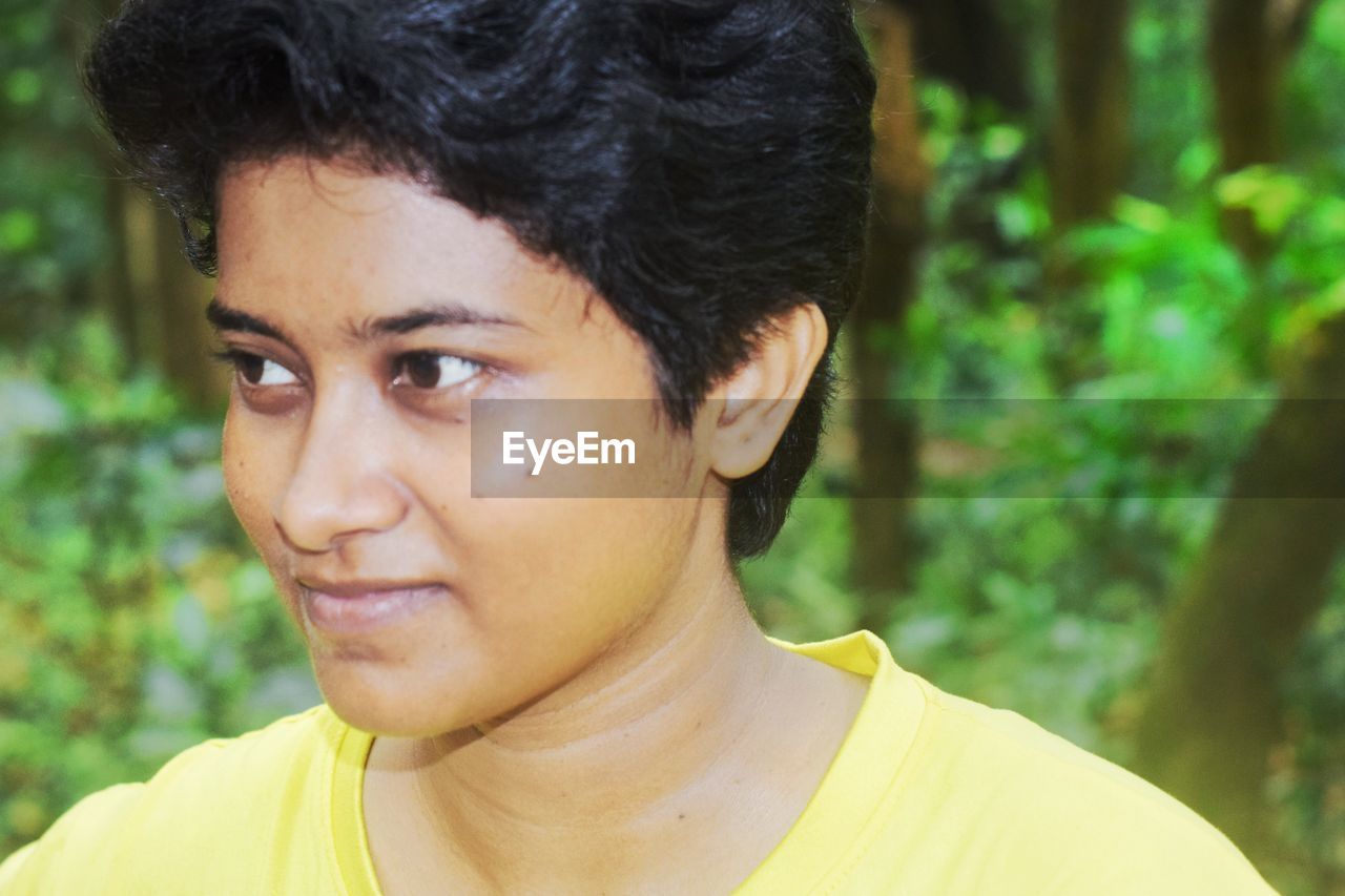 portrait, headshot, one person, human hair, hairstyle, teenager, human face, person, adult, men, black hair, young adult, emotion, forest, lifestyles, nature, close-up, looking, focus on foreground, yellow, looking at camera, human head, casual clothing, portrait photography, outdoors, front view, tree, day, smiling, serious, contemplation, photo shoot, happiness