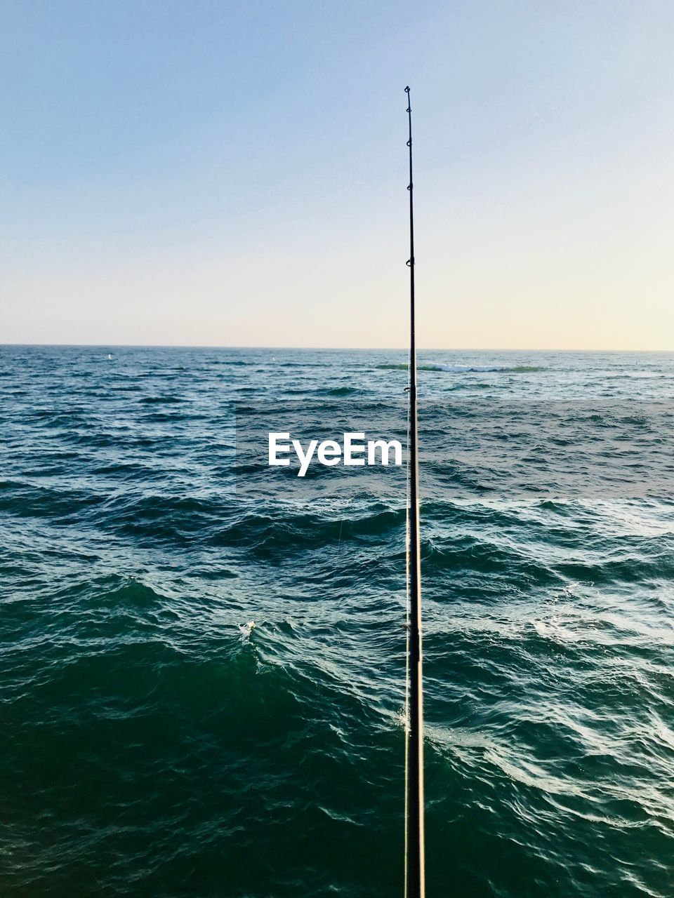 Fishing rod over sea against clear sky