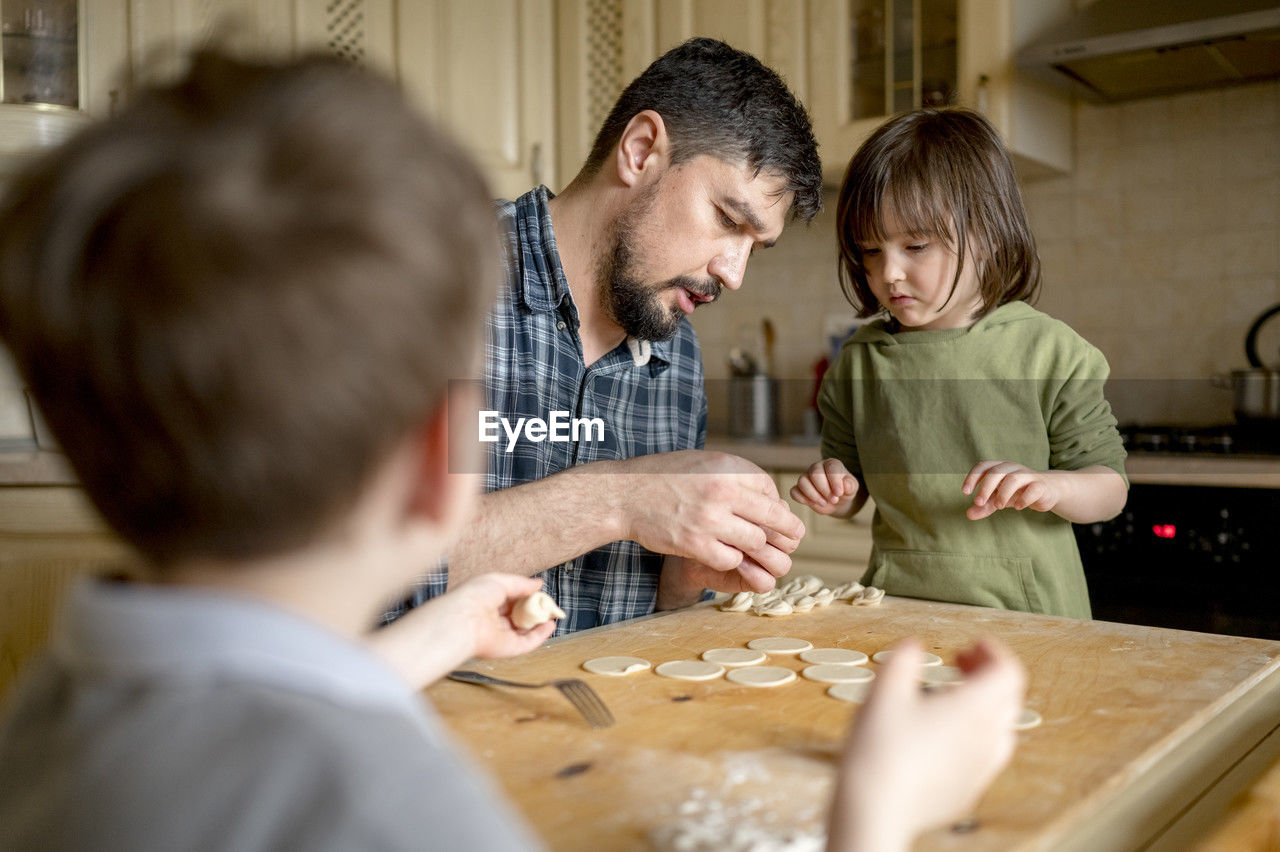 Father teaching children to make dumplings at kitchen