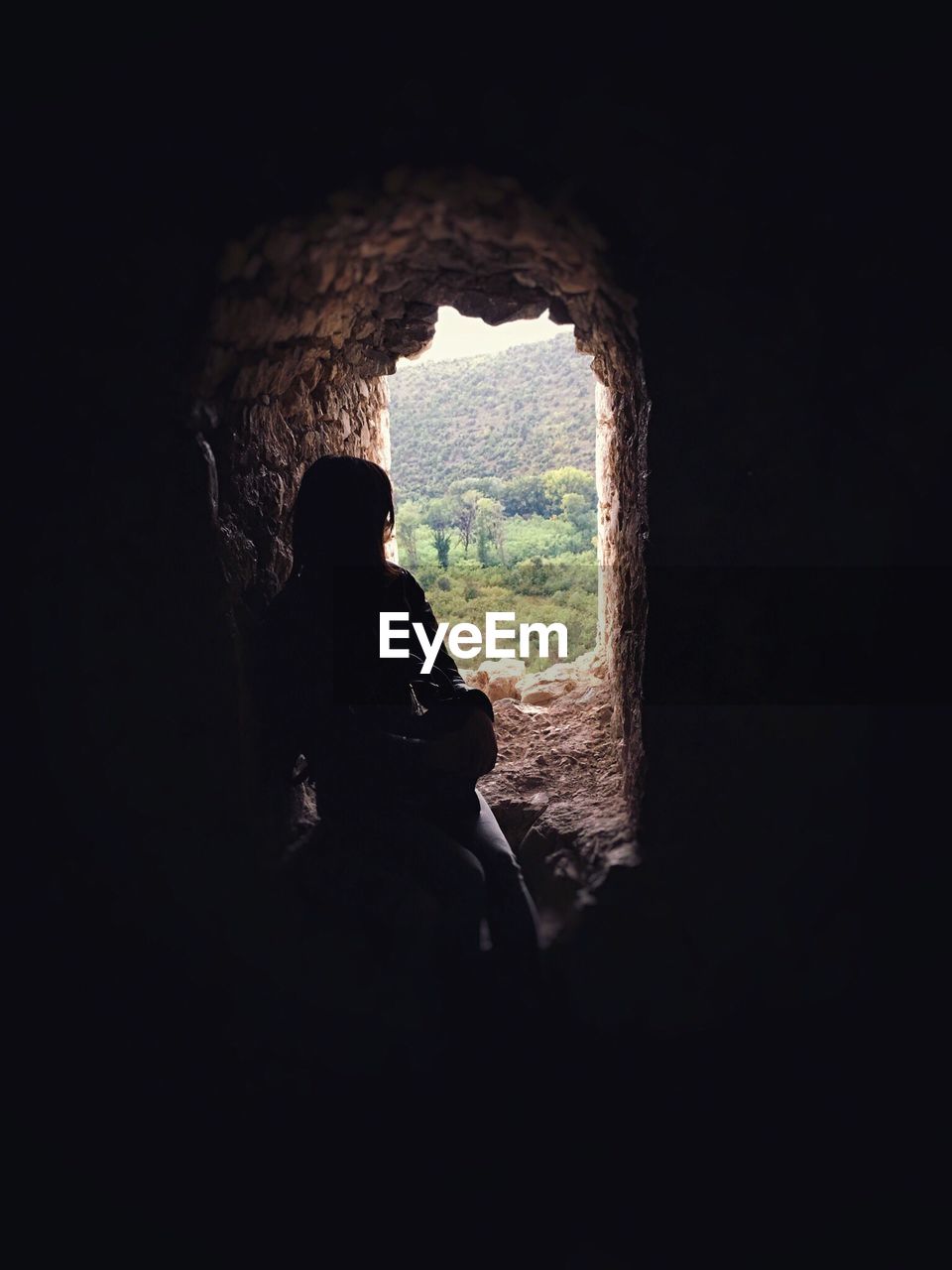 REAR VIEW OF SILHOUETTE WOMAN SITTING ON ROCK