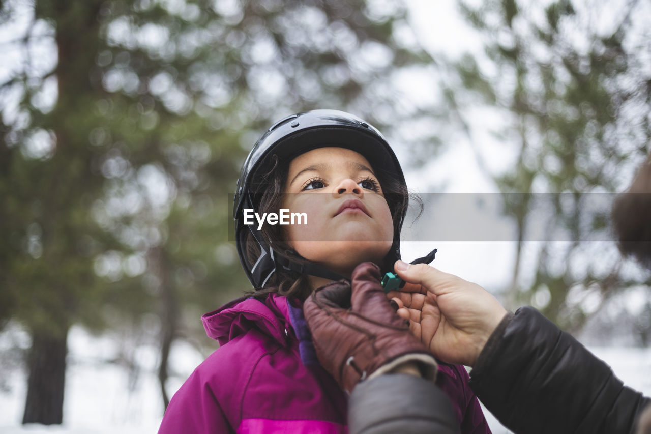 Mature man helping daughter wearing helmet during winter