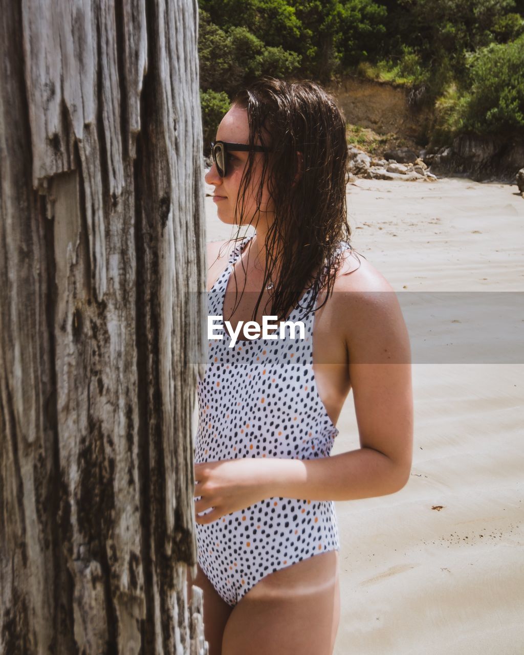 Young woman standing by tree trunk