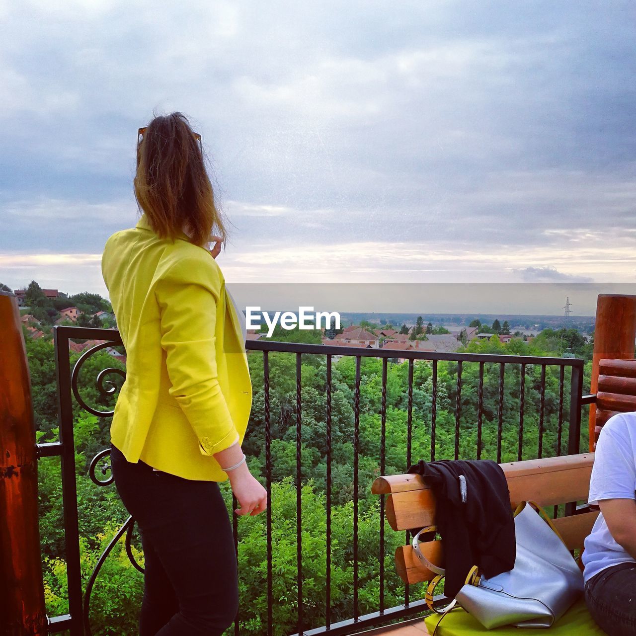 REAR VIEW OF WOMAN SITTING ON RAILING AGAINST SEA