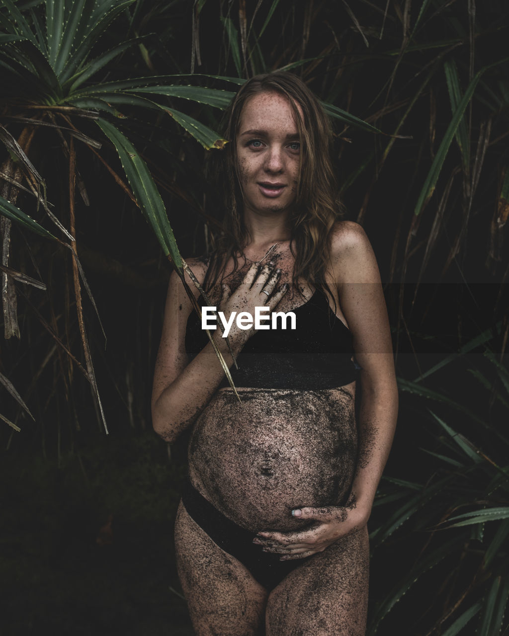 Portrait of smiling pregnant woman covered in dirt standing against plants